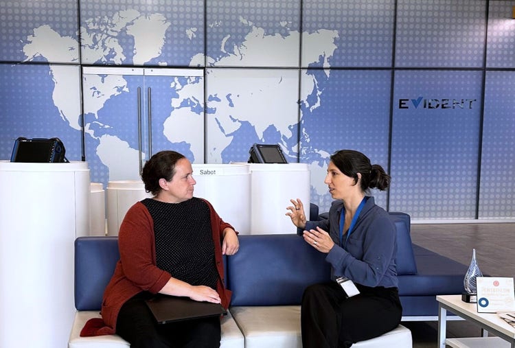 Emilie Peloquin NDT expert talking with her interviewer in front of a large world map on a wall with an Evident logo