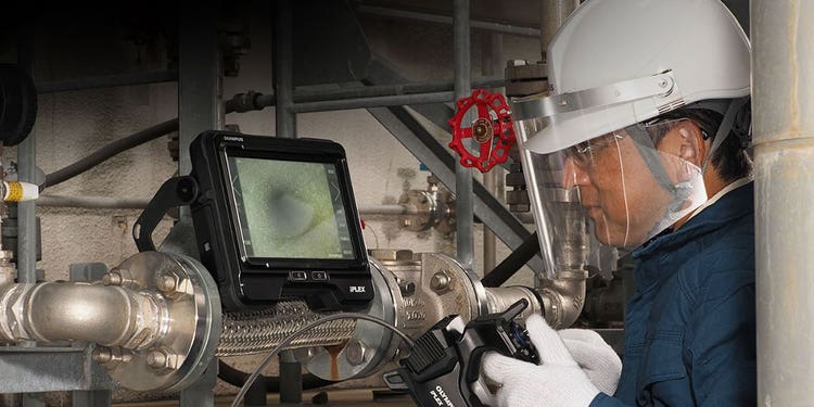 Videoscope set up on a pipe with an inspector wearing personal safety equipment using the hand controller to operate the insertion tube to inspect inside piping in an industrial plant