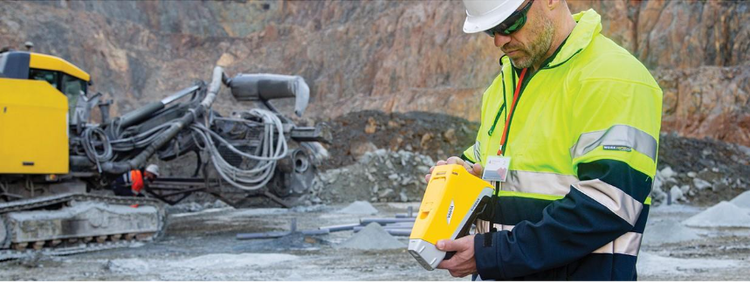 A person in a safety vest and hardhat looking at a device Description automatically generated