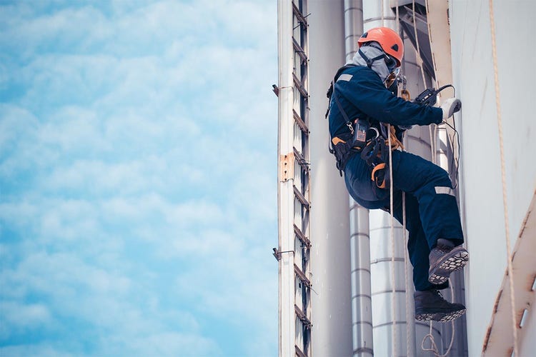 Trabajador dedicado a un trabajo de inspección vertical en cuerda para un tanque de almacenamiento industrial en el que se miden las chapas del forro exterior.