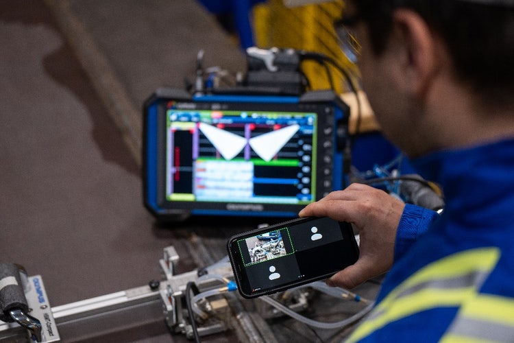 Inspection technician holding a smart phone with a zoom video conference on the screen and showing his scanner and OmniScan X3 configuration using the phone camera