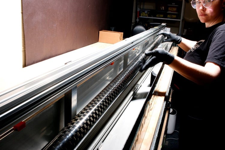 检测人员正在将一个碳纤维管放入用于检测管子的水浸槽中。