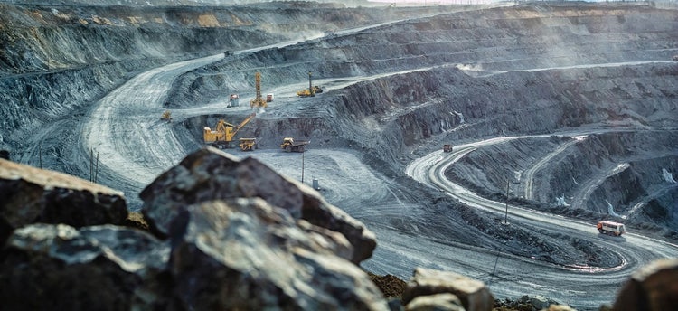 Open pit mine with mining equipment including trucks and excavator in the distance.